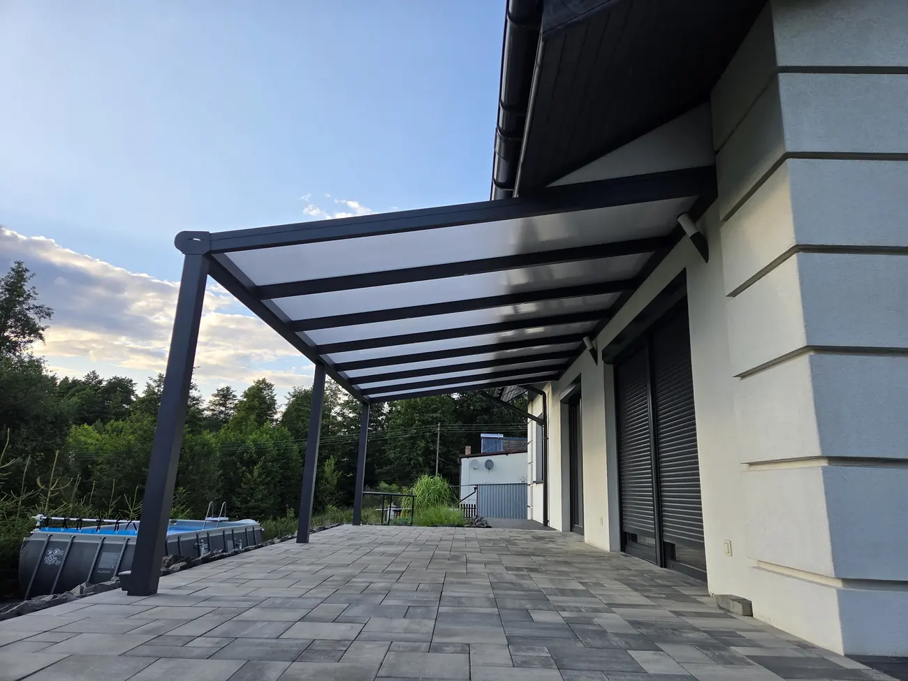 Hliníková pergola se střechou z polykarbonátu podél fasády domu