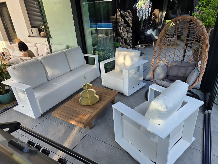 Zestaw ogrodowy z aluminium - sofa i dwa fotele z białymi poduszkami wokół teakowego stolika na tarasie