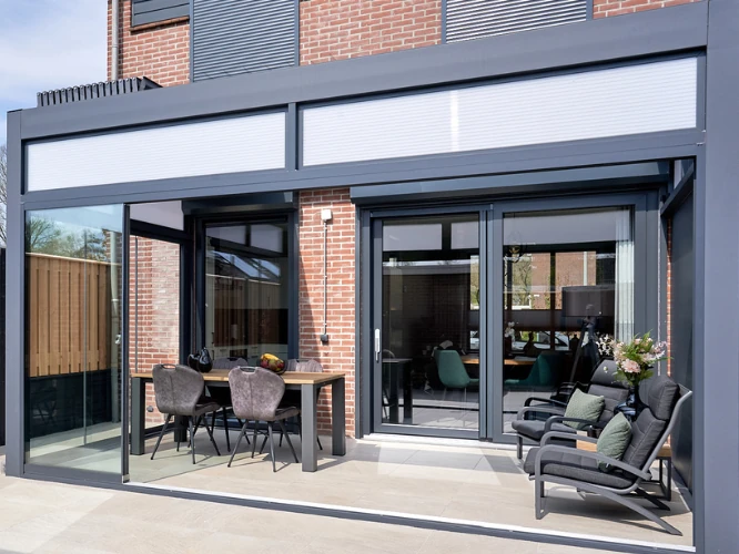 Pergola bioklimatyczna Pinela Deluxe z przesuwną zabudową szklaną przy domu jednorodzinnym