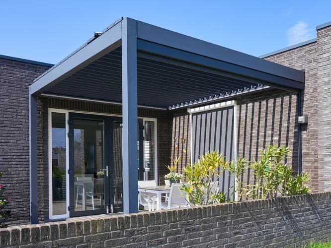Pergola bioklimatyczna Pinela z antracytowymi lamelami aluminiowymi nad tarasem przy domu jednorodzinnym