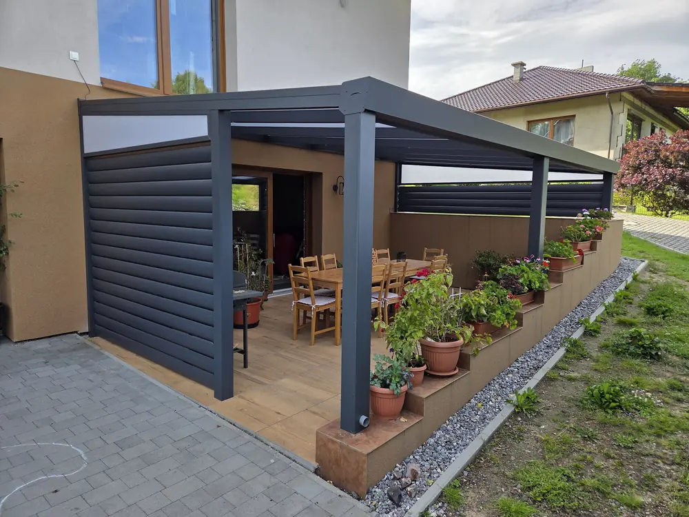 Aluminiowa pergola tarasowa z bocznymi osłonami roletowymi nad tarasem drewnianym